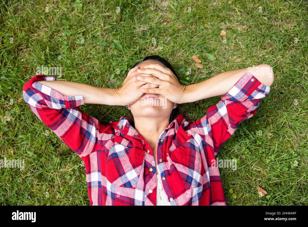 Femme couvrant les yeux avec les mains couchée sur l'herbe Banque D'Images
