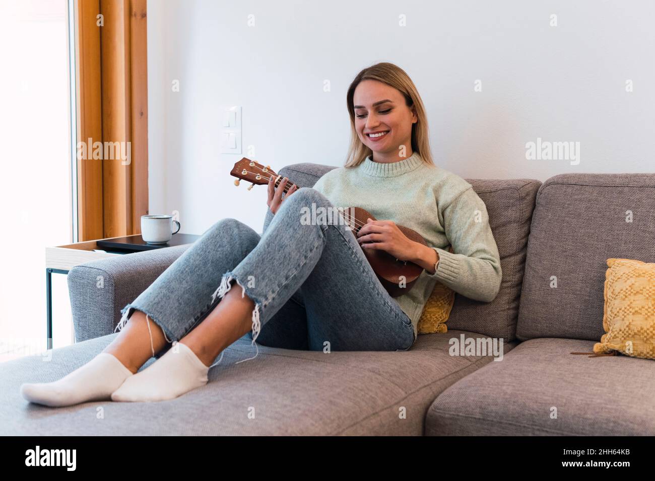 Femme souriante jouant ukulele assis sur un canapé à la maison Banque D'Images