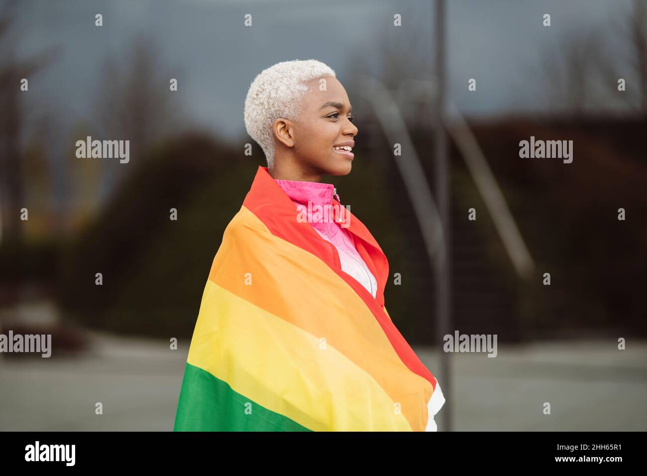 Femme LGBTQIA souriante enveloppée dans un drapeau arc-en-ciel Banque D'Images