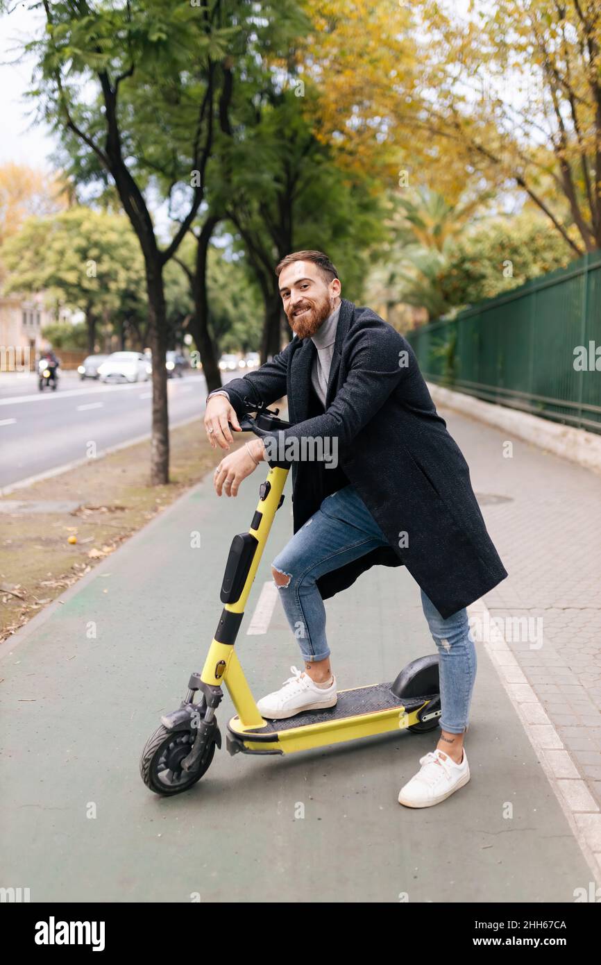 Un jeune homme souriant s'est penché sur un scooter électrique sur la piste cyclable Banque D'Images