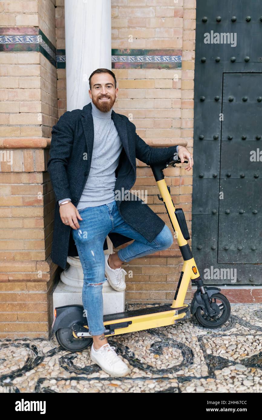 Joyeux barbu avec un scooter de poussée appuyé sur la colonne Banque D'Images