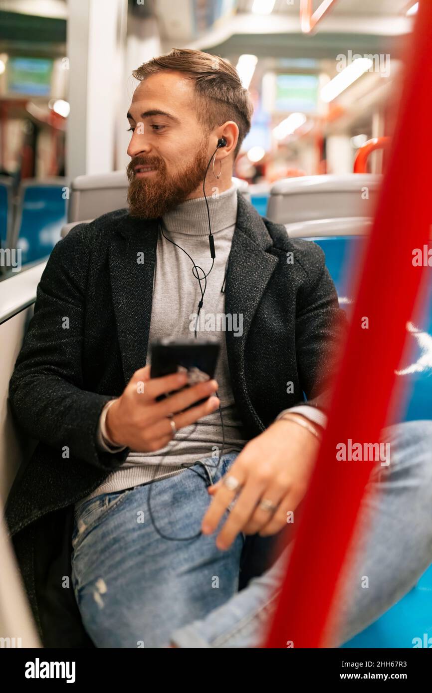 Un jeune homme écoute de la musique avec des écouteurs intra-auriculaires en tram Banque D'Images