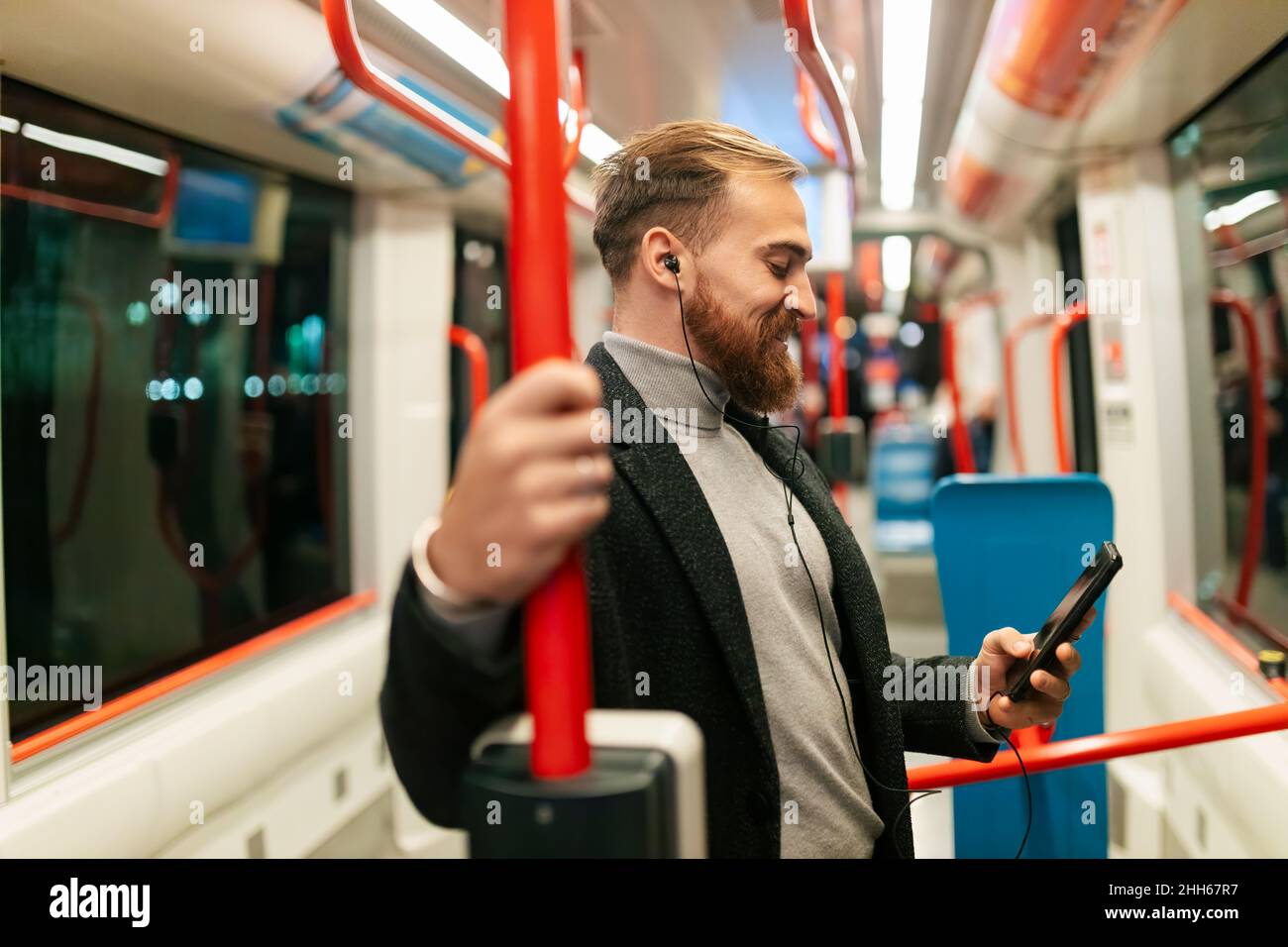Homme debout en tram avec un smartphone et en train d'écouter de la musique avec un casque intra-auriculaire Banque D'Images