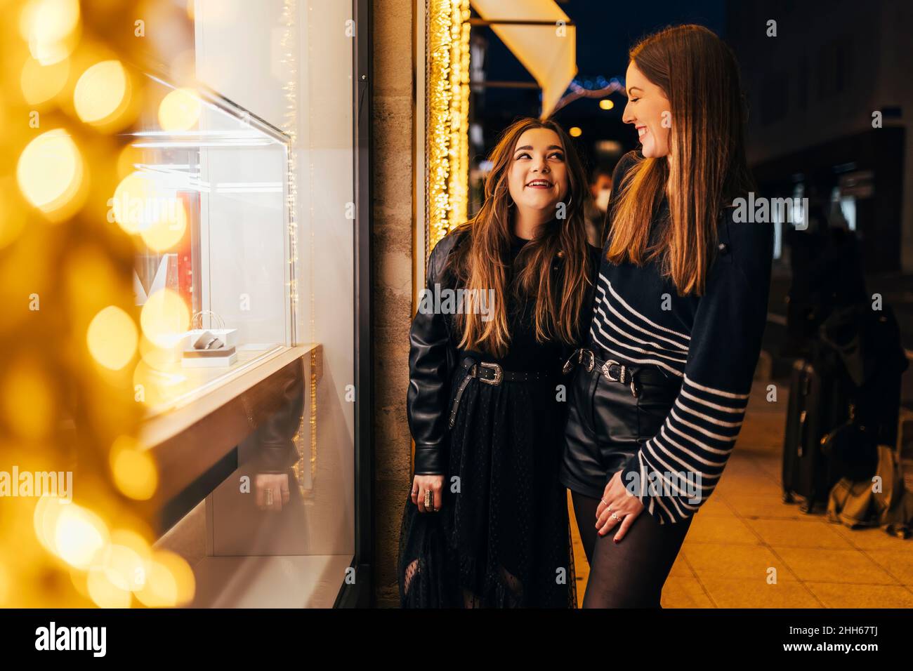 De jeunes amis souriants se tenant près de la fenêtre illuminée du magasin la nuit Banque D'Images