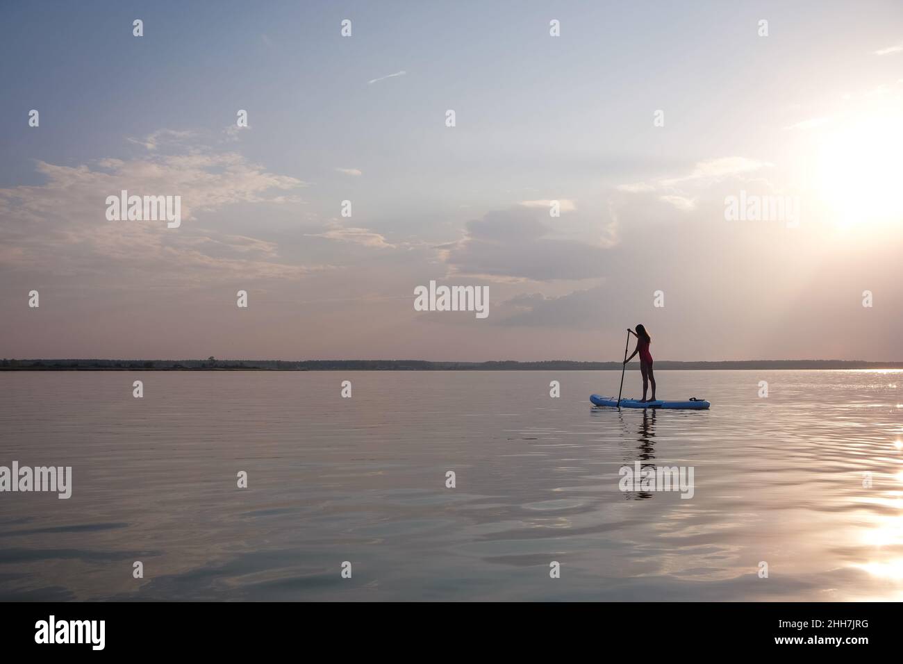 Silhouette de jeune femme paddle board au coucher du soleil. Banque D'Images