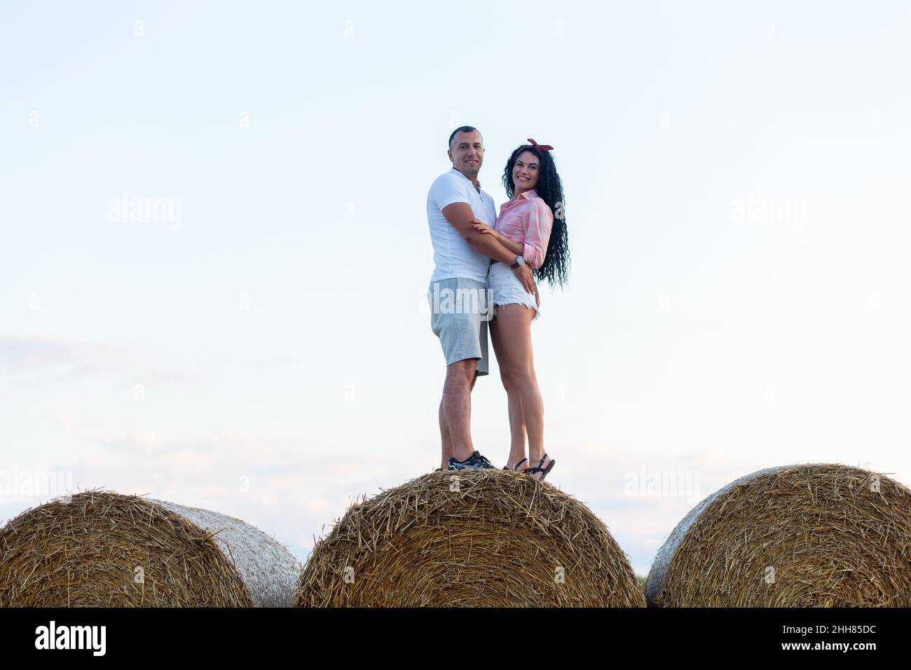 Couple aimant dans un champ sur des rouleaux de paille.Jeune homme et femme s'amusant, sautant et posant au coucher du soleil. Banque D'Images