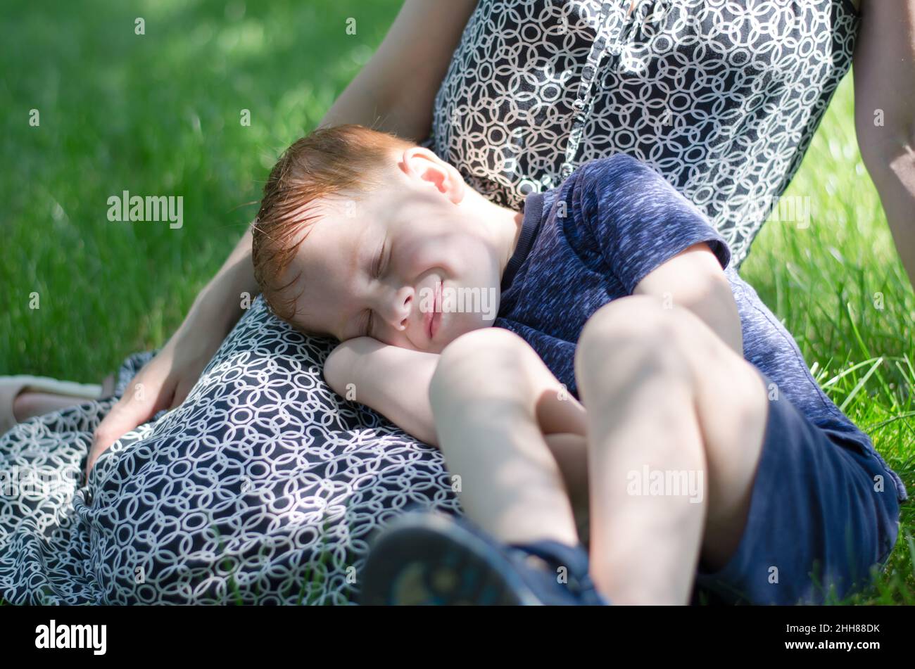 Les enfants dorment dans la nature.Un petit garçon dort sur les pieds de sa mère dans le parc. Banque D'Images