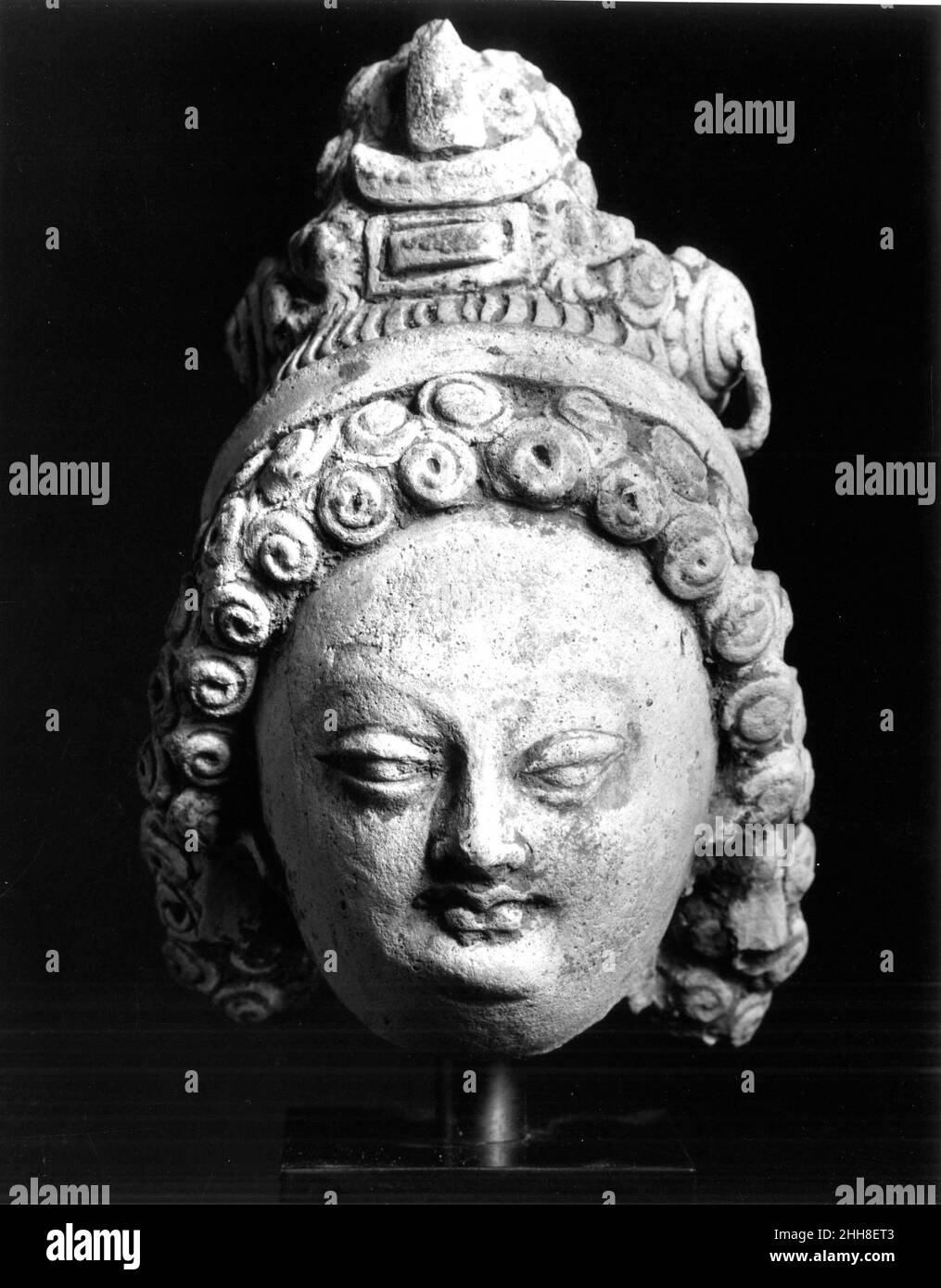 Tête 8th–10th siècle Chine les longs cheveux bouclés et les cocardes avec chaînes de suspension de chaque côté de la couronne sont souvent trouvés dans les représentations de bodhisattvas et de dévotés produits dans la région de Turfan et dans la région de Dunhuang dans le nord-ouest de la Chine du huitième au neuvième siècle.Tête.Chine.8th–10th siècle.Stuc avec des traces de dorure et de peinture.Sculpture Banque D'Images