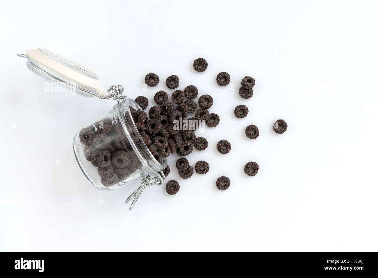 anneaux de maïs pour le petit déjeuner, savoureux anneaux noirs et céréales versés dans un pot en verre sur fond blanc, concept alimentaire saine Banque D'Images