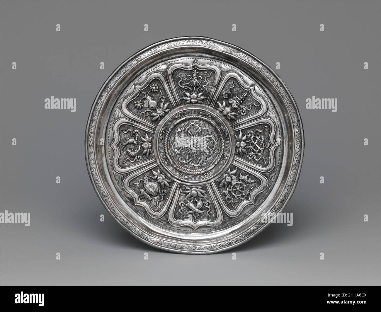 Stand de coupe avec les huit trésors bouddhistes Chine du 14th siècle les objets qui reposent sur des boutons de lotus à l'intérieur de ce stand de coupe représentent sept des huit trésors bouddhistes: Une roue, un nœud sans fin, une coquille de conch, une bannière de victoire, des fleurs de lotus,une paire de poissons et un vase au trésor.(Le huitième Trésor traditionnel, un parasol, a été remplacé ici par une paire de défenses d'éléphant.)Après le XIVe siècle, ces symboles, pas nécessairement dans un groupe de huit, sont apparus sur le travail des métaux, les porcellains et les textiles en Chine et au Tibet.Stand de tasse avec les huit trésors bouddhistes.Chine.14th c Banque D'Images