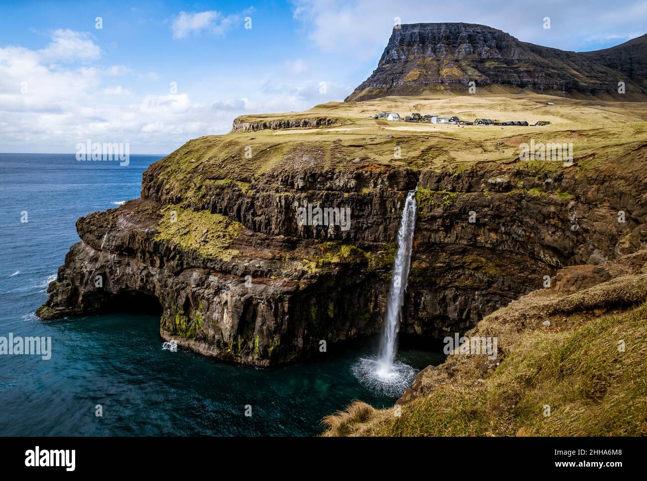 Une chute d'eau descend en cascade sur un spectaculaire front de roche jusqu'à une zone d'eau blanche sauvage.Un village se trouve au-dessus de la plage, niché dans une pelouse vert pâle. Banque D'Images