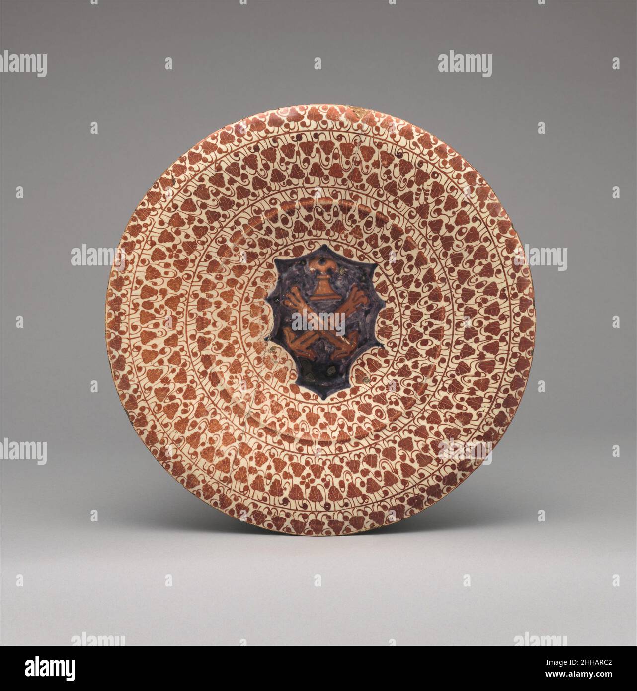 Plaque 1430–1470 espagnole cette plaque est ornée des armoiries de la famille Morelli de Florence, et doit avoir appartenu à un grand service de table.Cette petite assiette, en raison de sa taille, a probablement été utilisée principalement pour manger.Des exemples de services de jumelage n'ont que rarement survécu, bien que des documents indiquent que de grands nombres ont été faits pour les marchés nationaux et les marchés d'exportation.Dans un reçu en date de 1454, la veuve de Don Pedro Buyl, surcorde des usines de lusterware de Manises, a reçu le paiement de 6000 gueldos (environ l'équivalent de $360 000 en 2016) en tant que dîme sur le dest des biens des potiers Banque D'Images