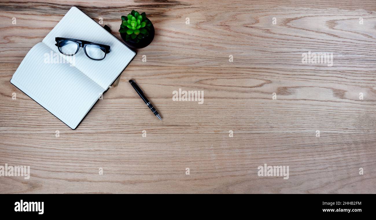 Table de bureau en chêne avec papier, stylo, lunettes de lecture et usine de fournitures de travail.Vue de dessus avec espace de copie au format de mise à plat. Banque D'Images