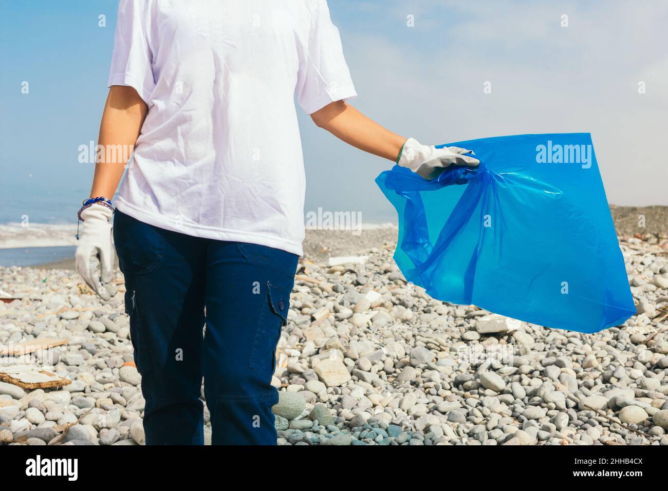 Une femme avec un sac bleu vide sur une plage de galets Banque D'Images