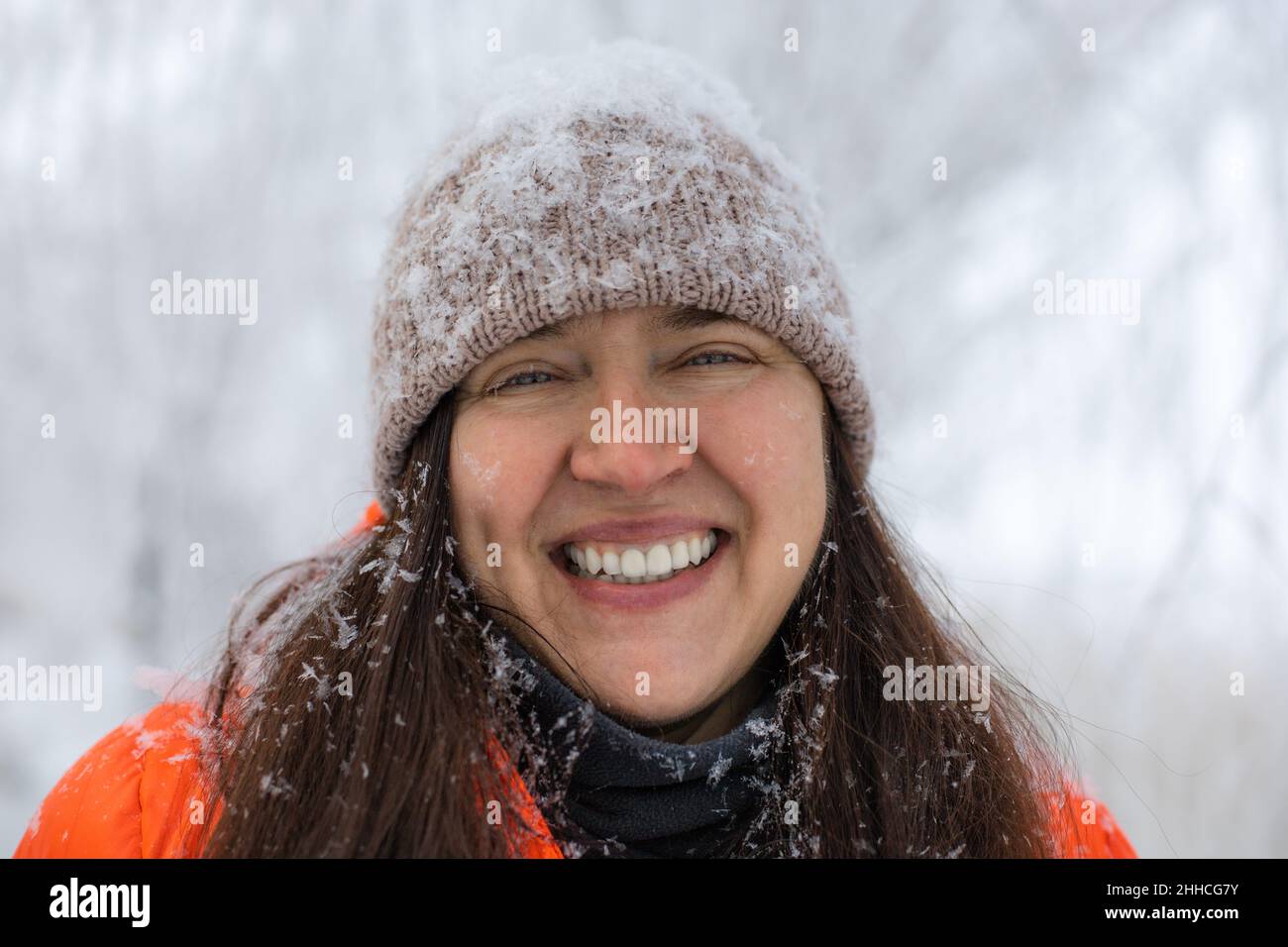 Portrait d'une femme d'âge moyen qui regarde l'appareil photo en souriant avec des dents portant des vêtements chauds d'hiver avec un chapeau et des cheveux couverts de neige.Charmant Banque D'Images