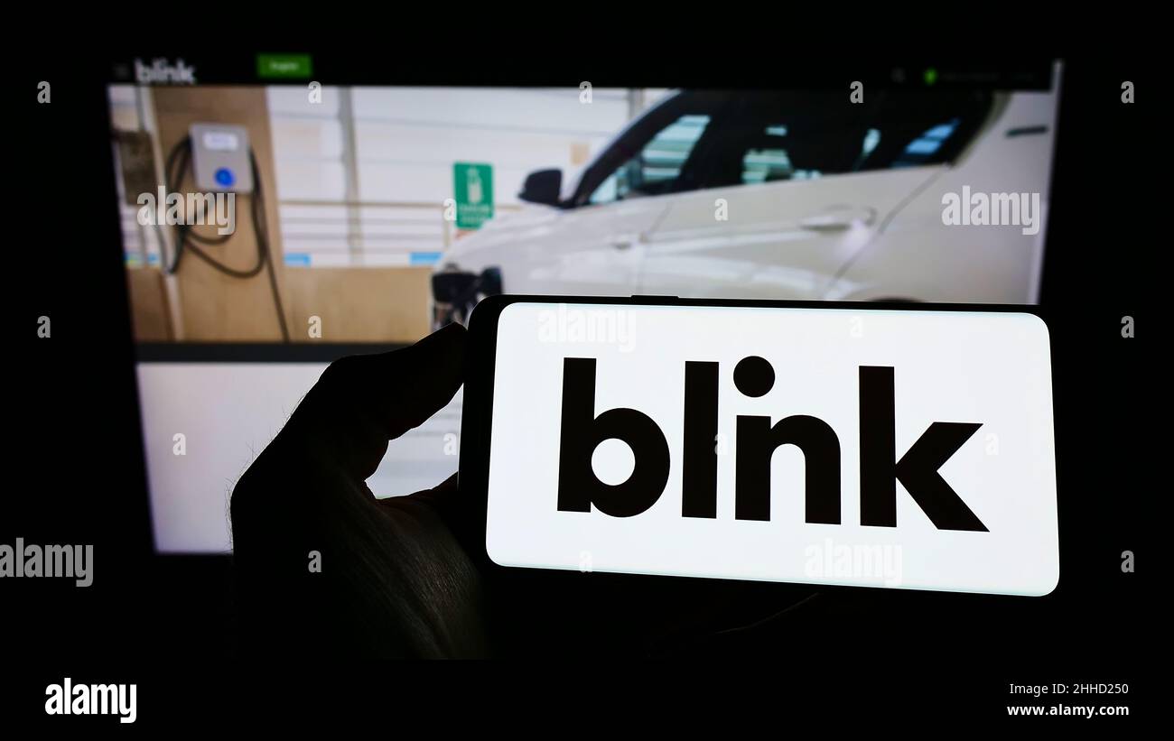 Personne tenant un téléphone portable avec le logo de la société américaine Blink Charging Co. Sur l'écran en face de la page Web d'affaires.Mise au point sur l'affichage du téléphone. Banque D'Images Personne tenant un téléphone portable avec le logo de la société américaine Blink Charging Co. Sur l'écran en face de la page Web d'affaires.Mise au point sur l'affichage du téléphone. Banque D'Images