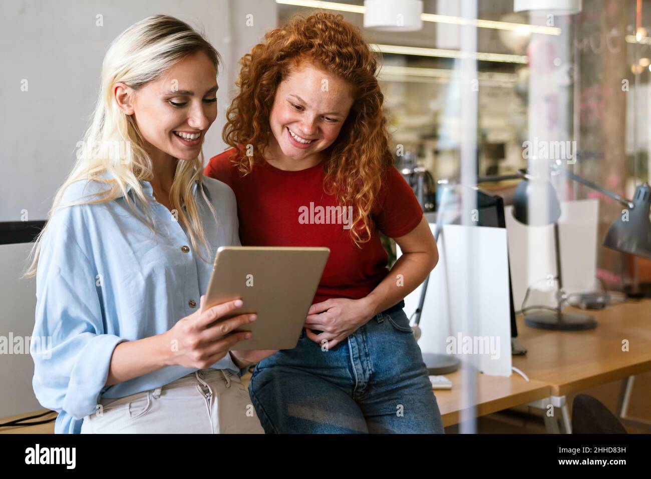 Des femmes d'affaires souriantes travaillant ensemble en ligne sur une tablette au bureau Banque D'Images