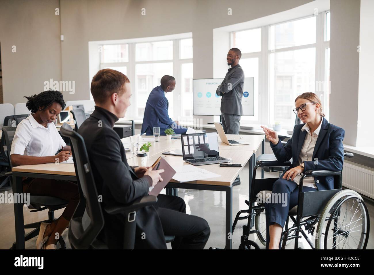 Divers groupes de gens d'affaires à la table de réunion au bureau avec une femme en fauteuil roulant en premier plan Banque D'Images