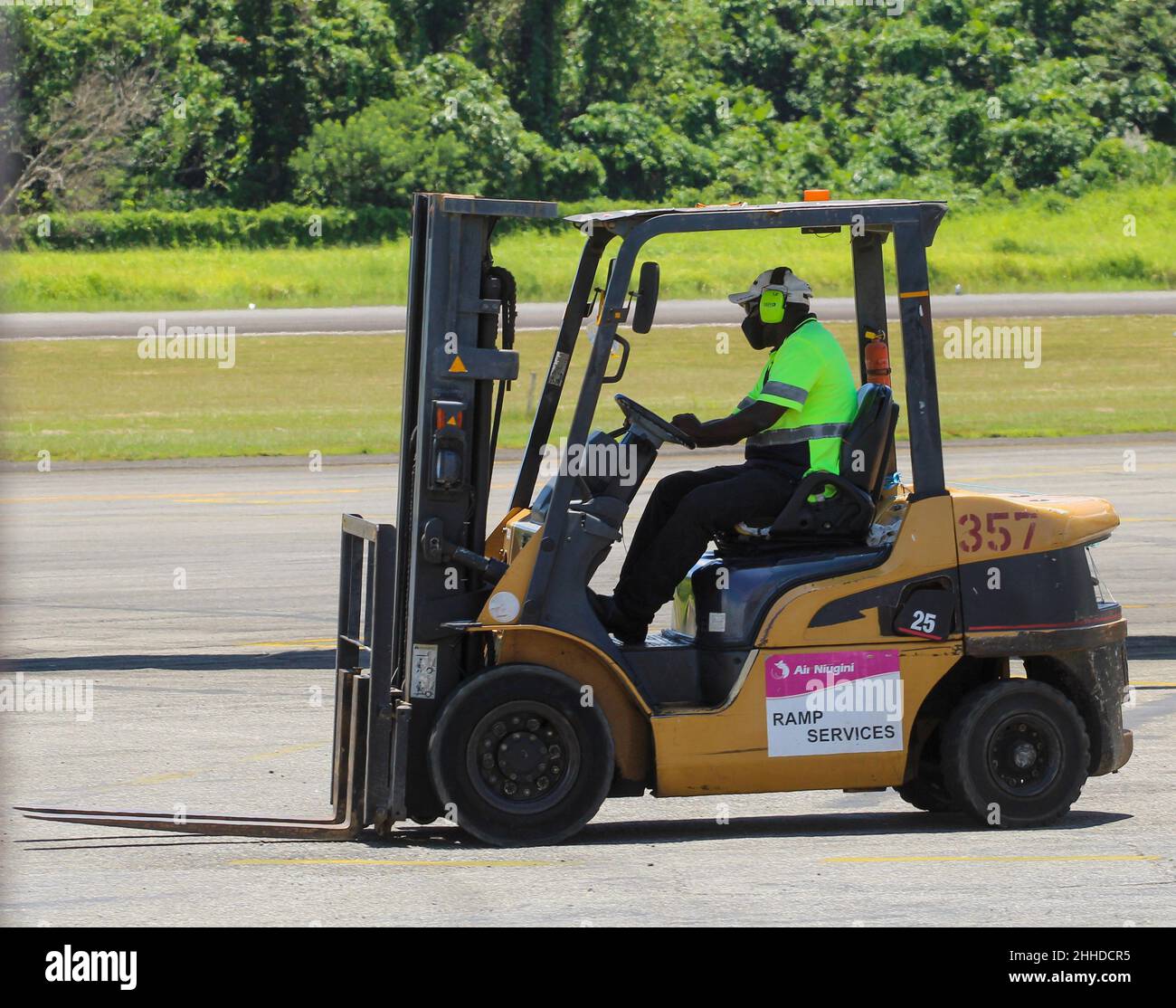 Un employé d'Air Niugini Ramp services dans un équipement de sécurité conduit un chariot élévateur jaune sur le tarmac de l'aéroport de Madang. Banque D'Images