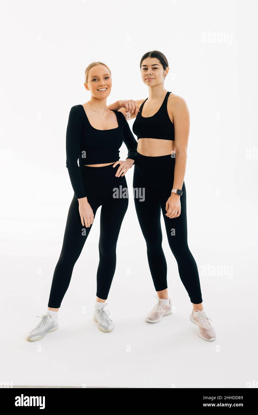 Deux femmes vêtues de sport portent des liens l'une avec l'autre tout en se tenant à l'intérieur sur fond blanc.Concept de personnes, d'exercice et de sport Banque D'Images