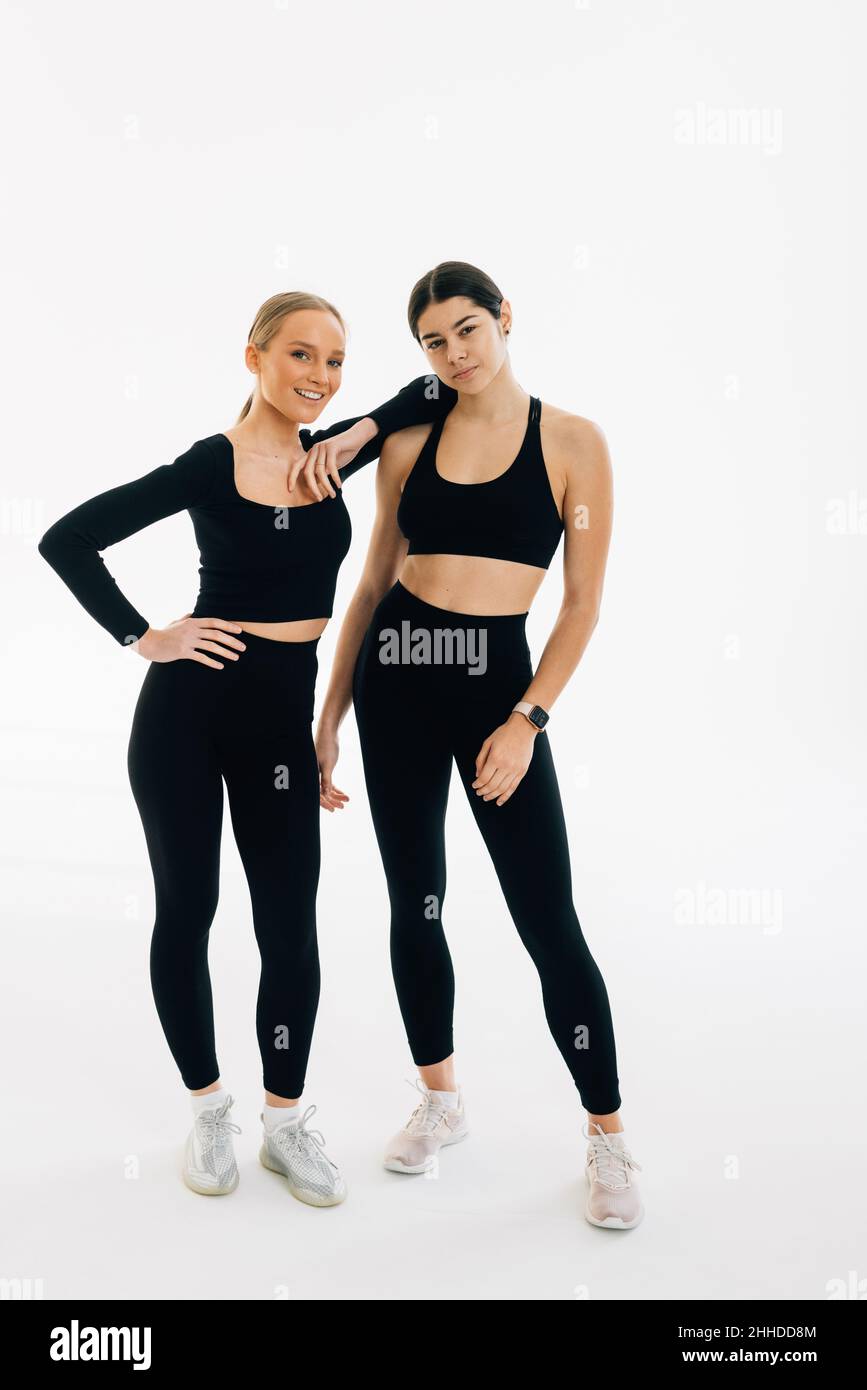 Deux femmes vêtues de sport portent des liens l'une avec l'autre tout en se tenant à l'intérieur sur fond blanc.Concept de personnes, d'exercice et de sport Banque D'Images