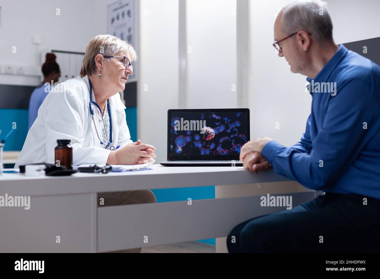Le médecin et le patient discutent de l'illustration du coronavirus sur l'ordinateur portable.Généraliste utilisant un ordinateur pour expliquer la représentation visuelle de la bactérie Covid 19 à l'homme âgé. Banque D'Images