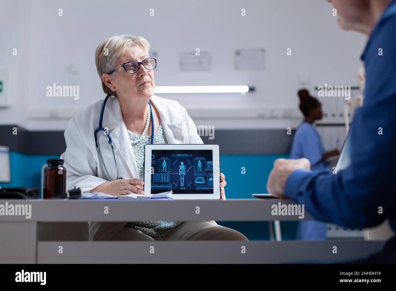 Spécialiste expliquant l'analyse du corps humain sur une tablette à un homme atteint d'une maladie lors de la visite de contrôle.Femme médecin et homme parlant de diagnostic avec l'illustration de l'anatomie sur l'appareil numérique. Banque D'Images