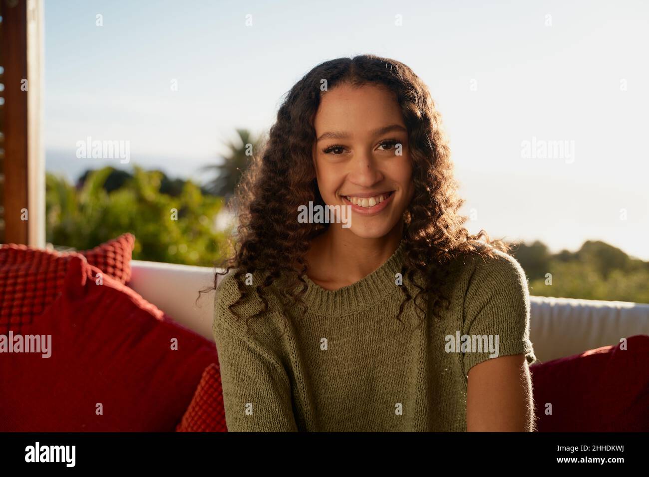 Portrait de la femme multiculturelle souriant tout en étant assis sur un canapé dans le salon de l'appartement moderne Banque D'Images