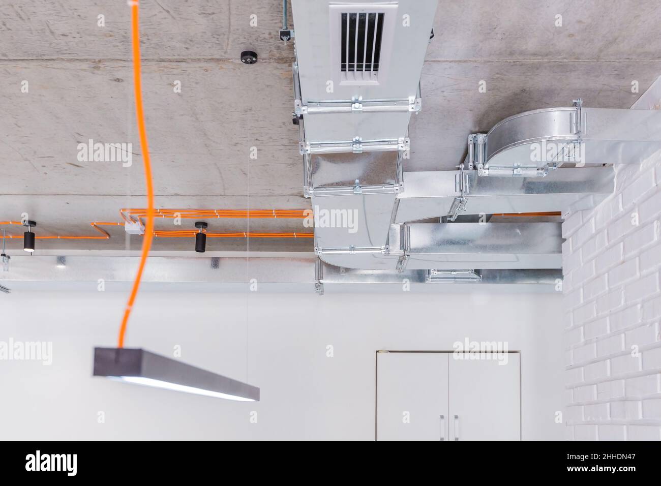 Plafond en béton avec câblage électrique orange et luminaires avec conduits de ventilation Banque D'Images