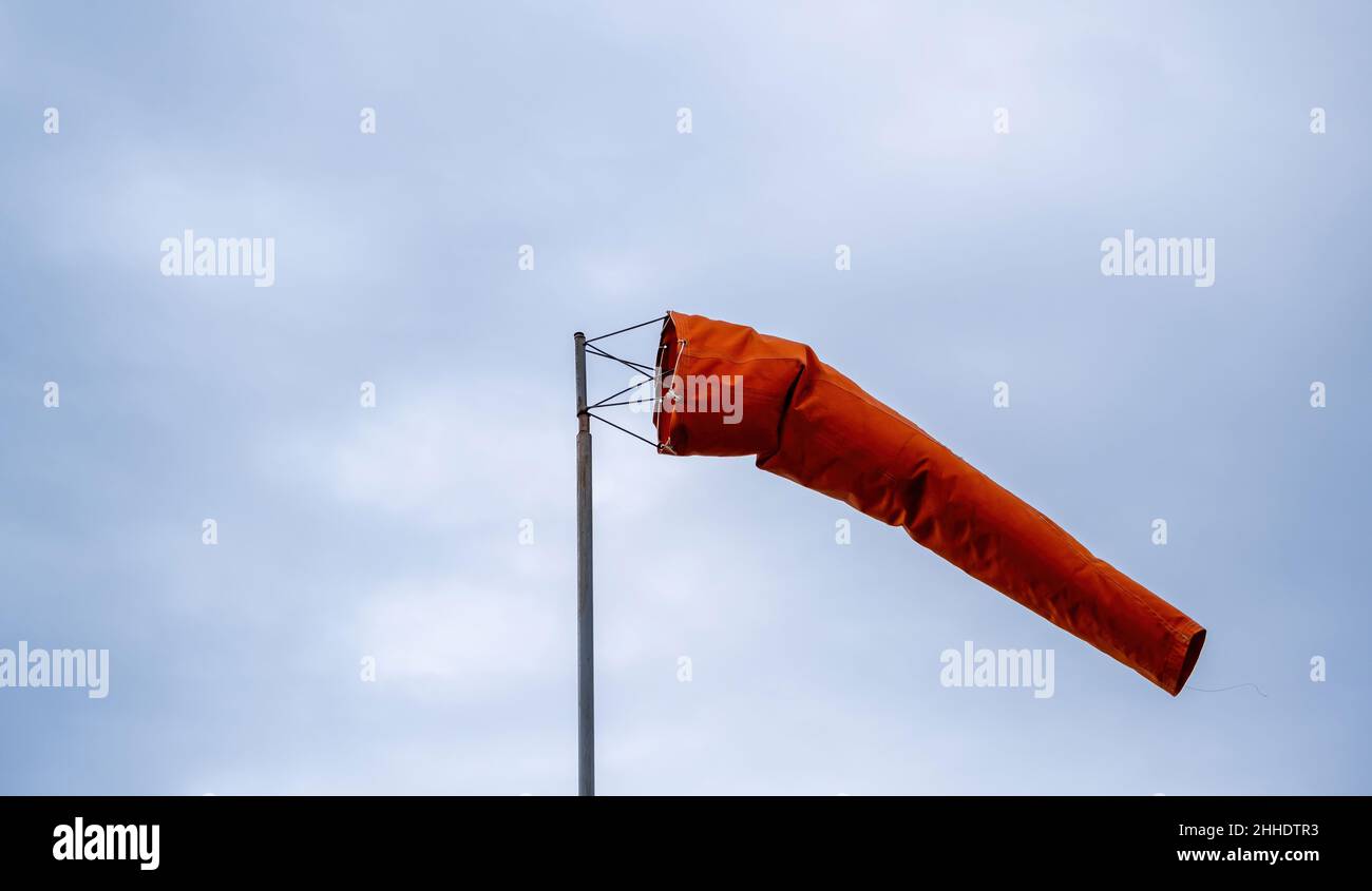 Chaussette de vent soufflant sur ciel nuageux.Cône rouge, indicateur de vitesse et de direction du vent.Journée venteuse à l'aéroport. Banque D'Images