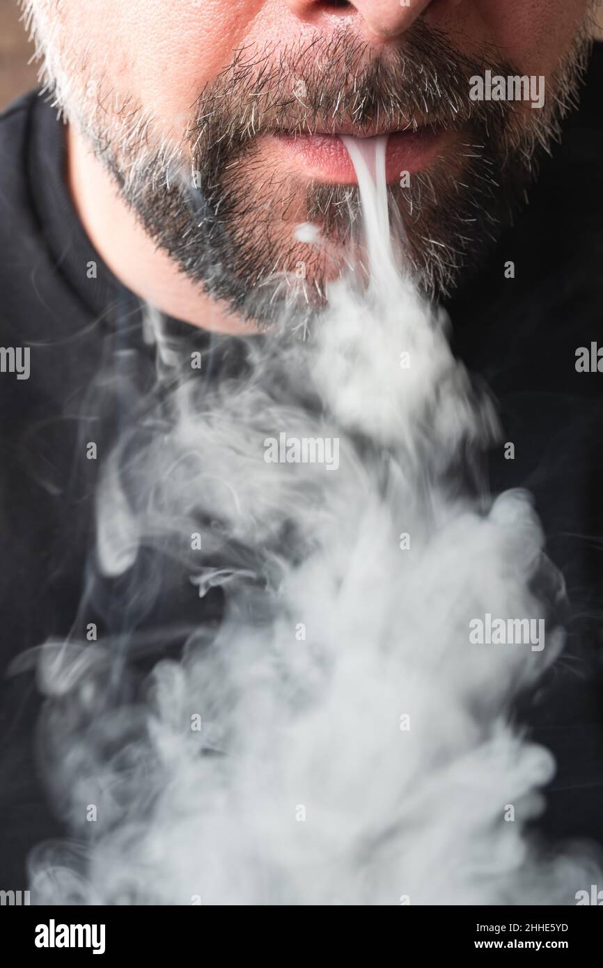 Gros plan d'une bouche soufflant de la fumée de cigarette grise. Banque D'Images