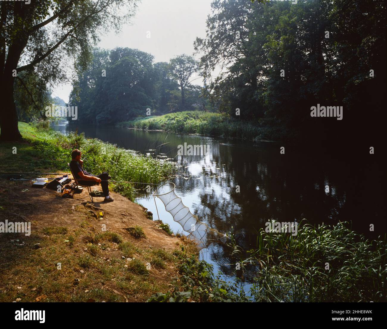 Pêcheur sur la rive de la rivière Avon Chippenham Wiltshire Angleterre Royaume-Uni arbres verts d'été et feuillage Banque D'Images