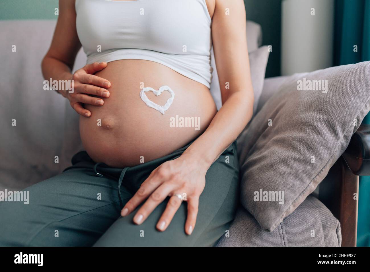 Femme enceinte méconnaissable avec cœur en hydratant sur le ventre Banque D'Images