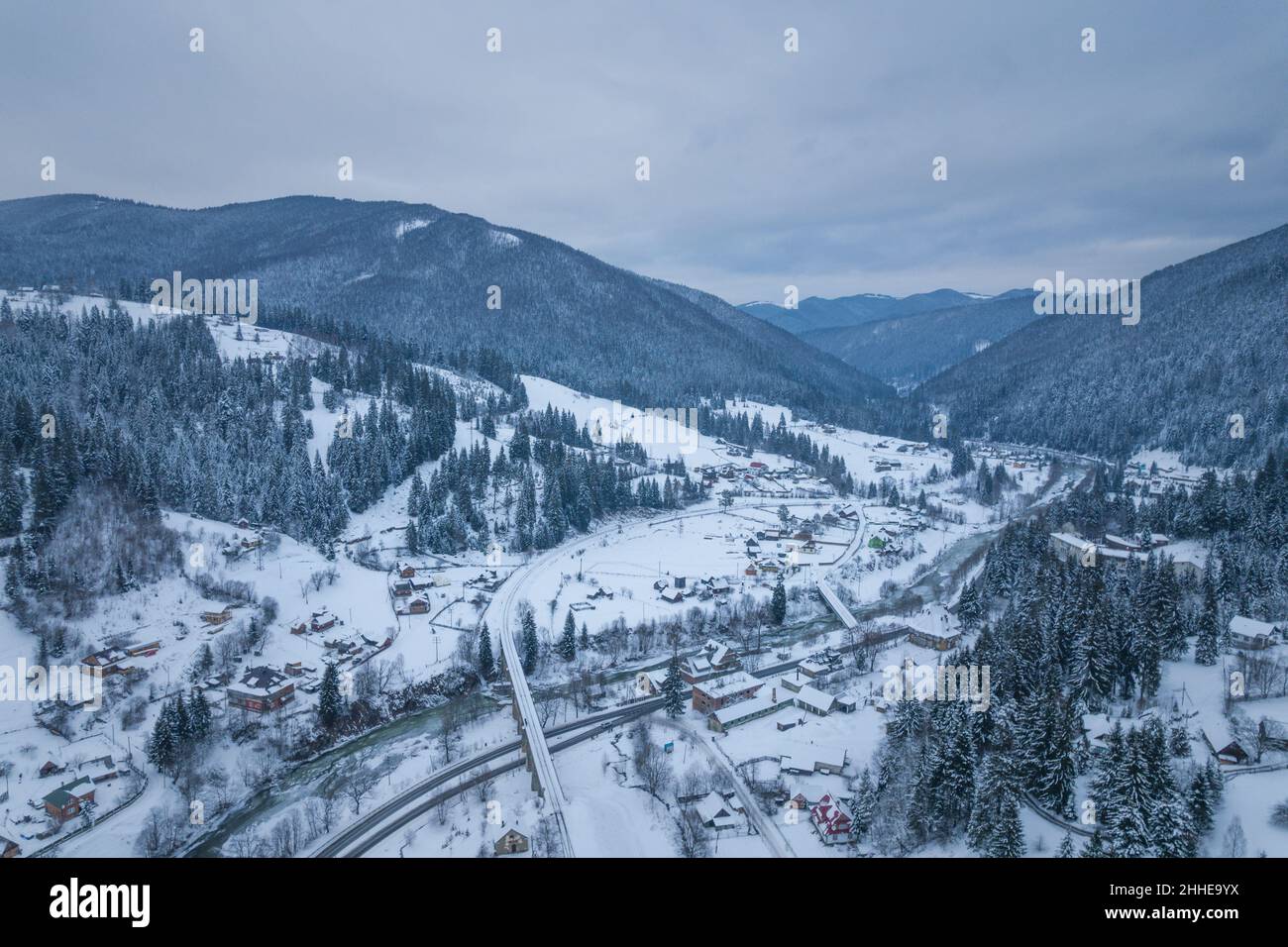 Une vallée avec un village entouré de montagnes et de forêt.Temps d'hiver sombre. Banque D'Images