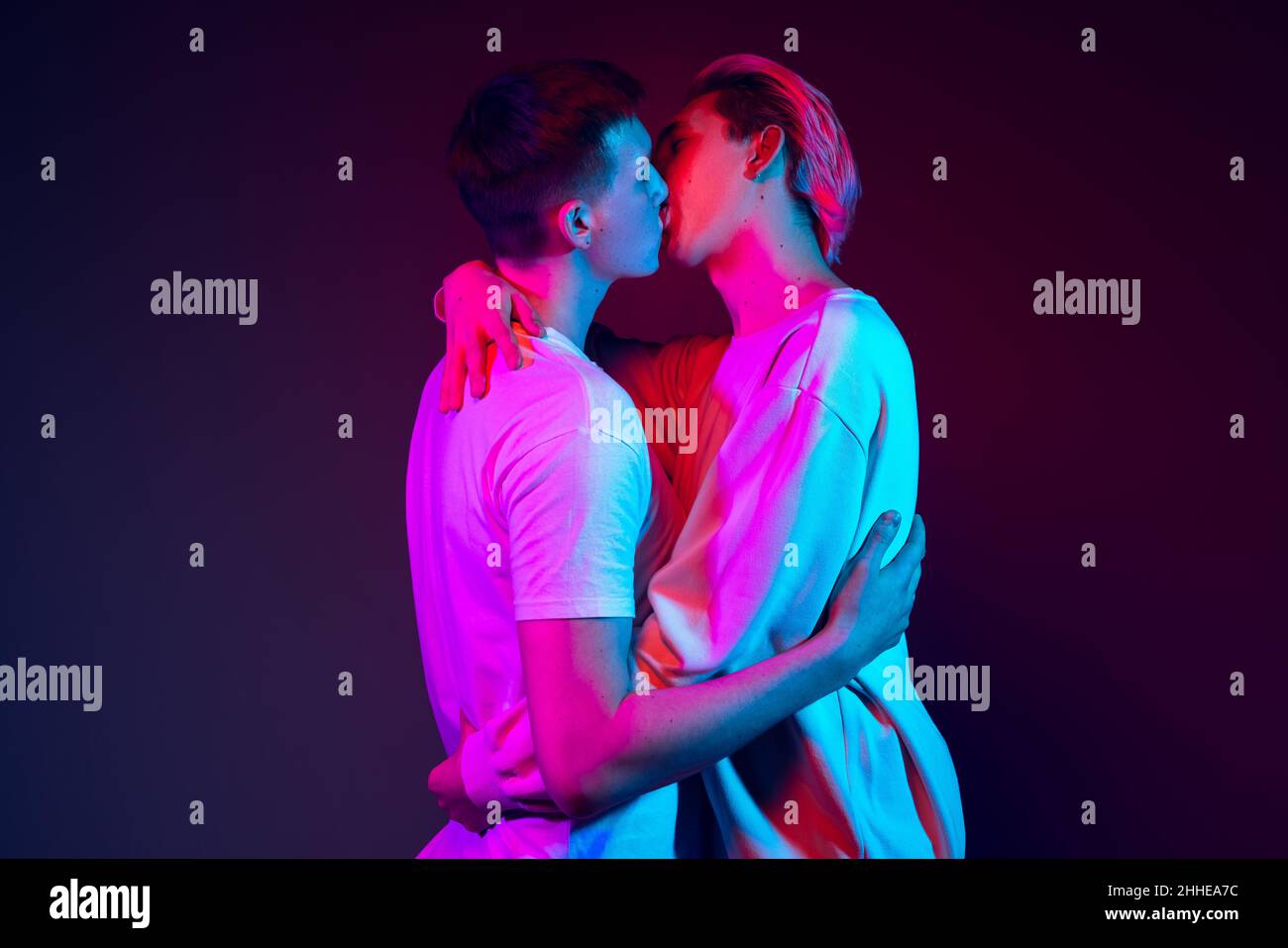 Gros plan deux jeunes hommes, couple embrassant isolé sur fond bleu à la lumière du néon.Concept des émotions, de l'amour, des relations, des droits de l'homme Banque D'Images