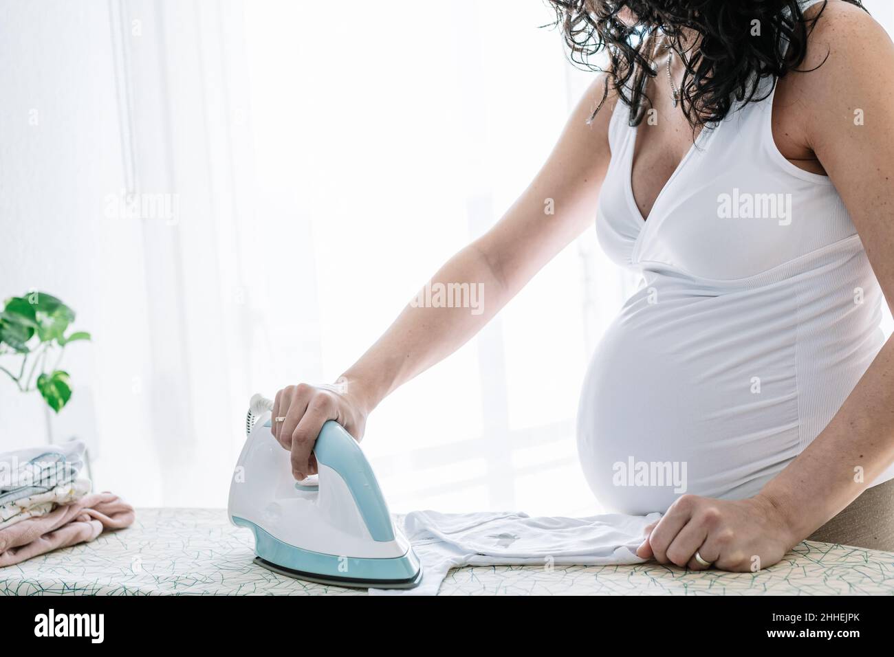 femme enceinte repassant et pliant les vêtements de son bébé, préparant la chambre pour l'arrivée future du nouveau-né Banque D'Images