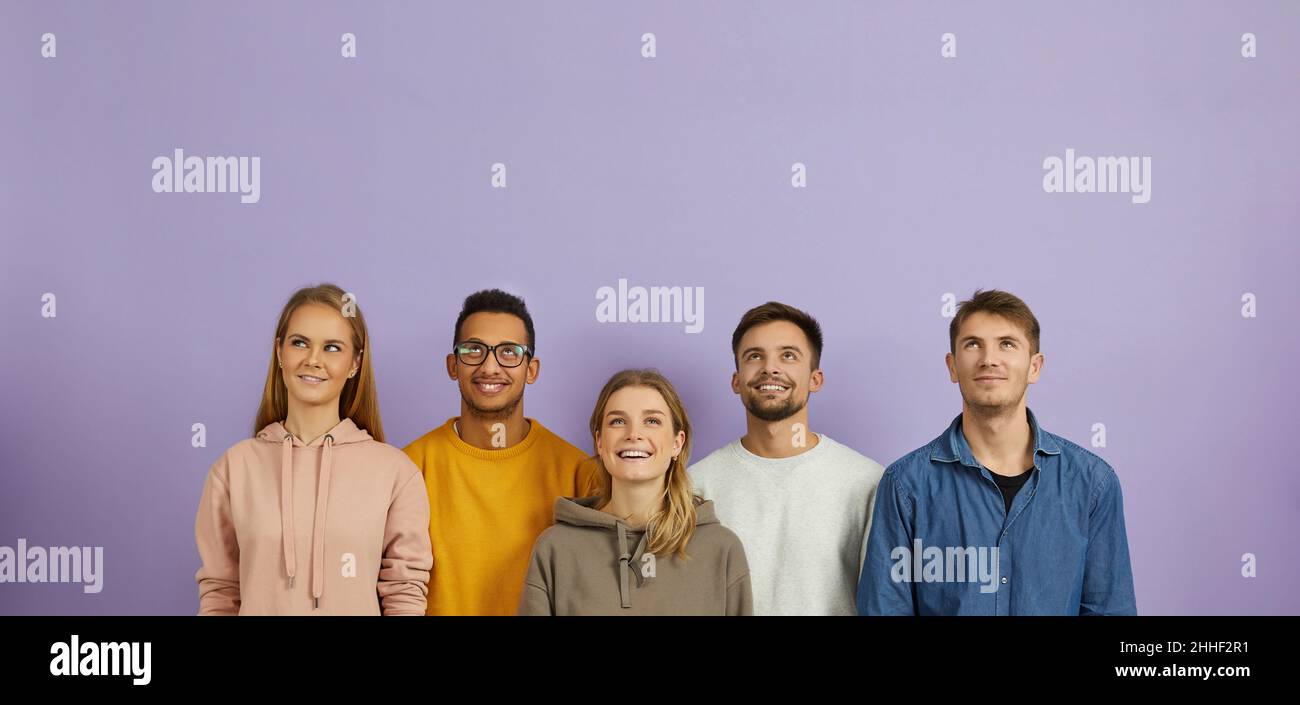 Des jeunes gens multiraciaux heureux debout sur fond violet, regardant vers le haut et souriant Banque D'Images
