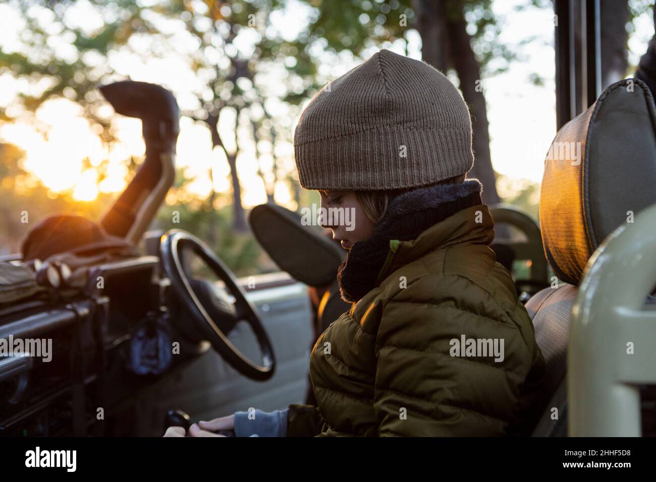 Un garçon dans un chapeau et un manteau en jeep au lever du soleil lors d'un safari. Banque D'Images