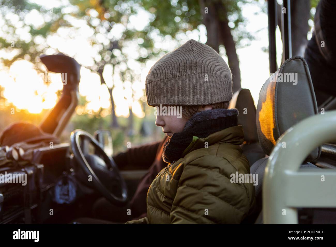 Un garçon dans un chapeau et un manteau en jeep au lever du soleil lors d'un safari. Banque D'Images