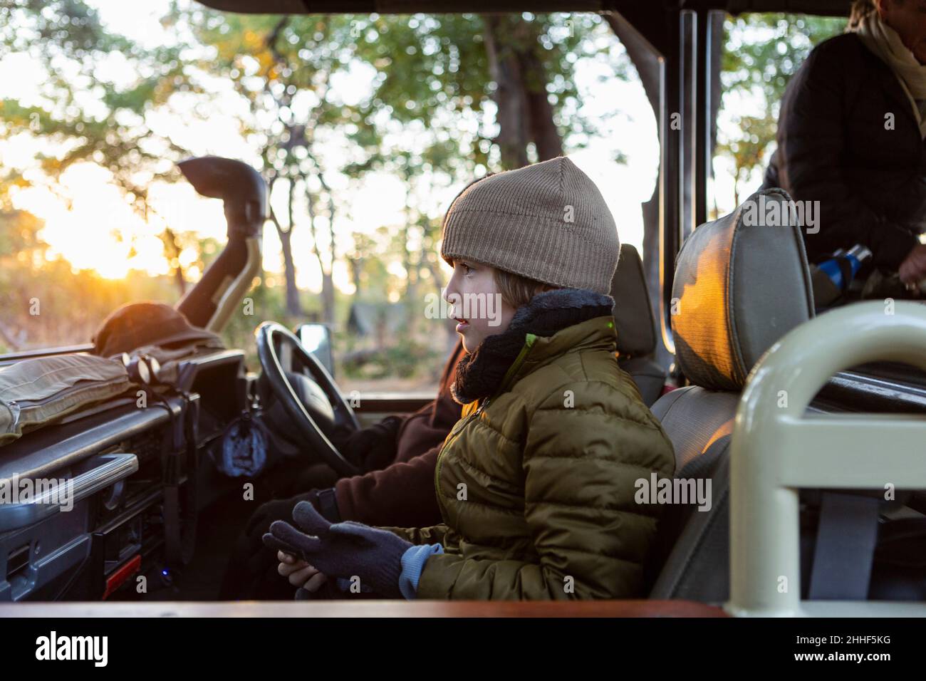 Un garçon dans un chapeau et un manteau en jeep au lever du soleil lors d'un safari. Banque D'Images