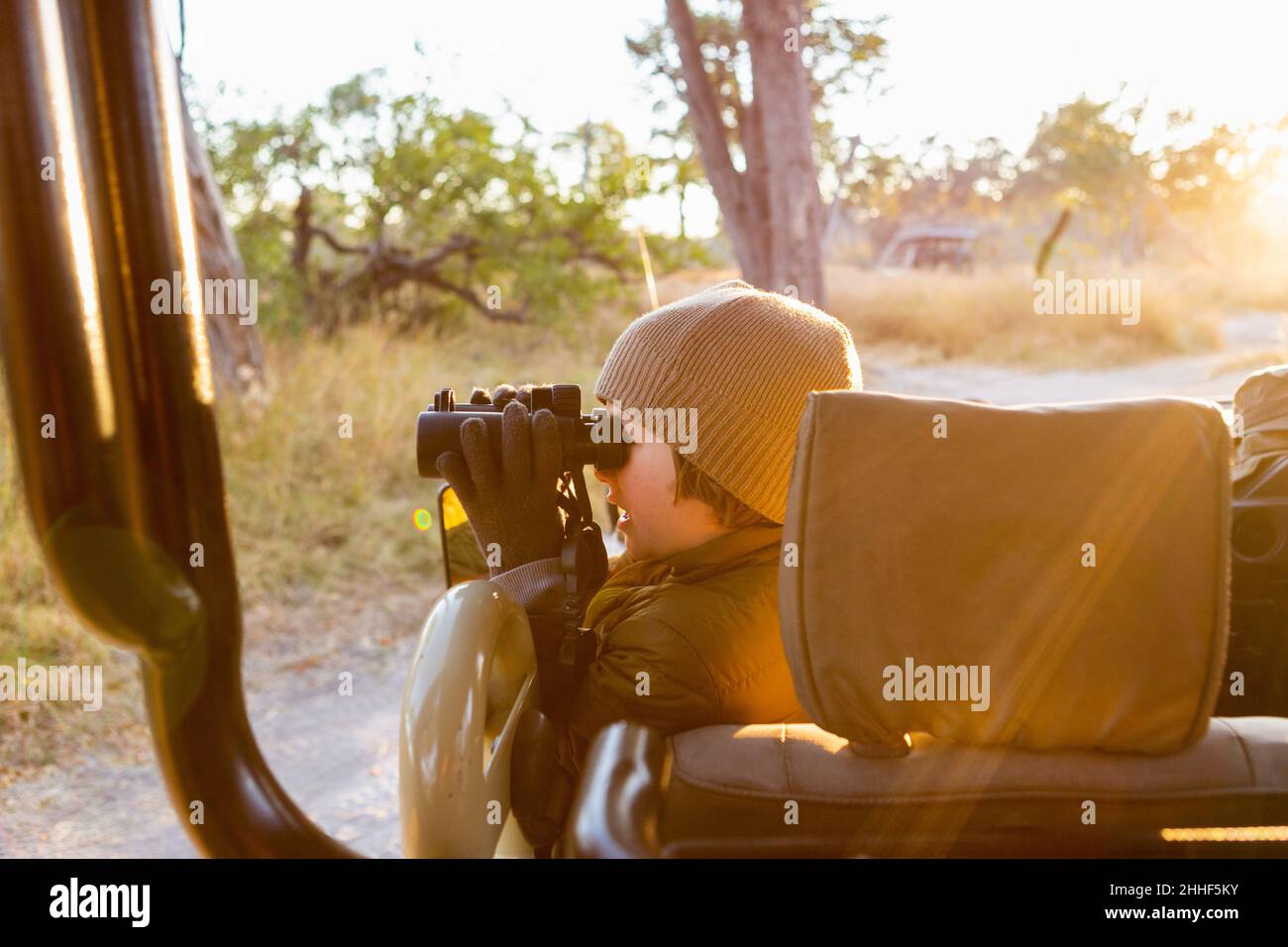 Jeune garçon dans une jeep à l'aide de jumelles, une voiture à l'aube à travers le Bush. Banque D'Images