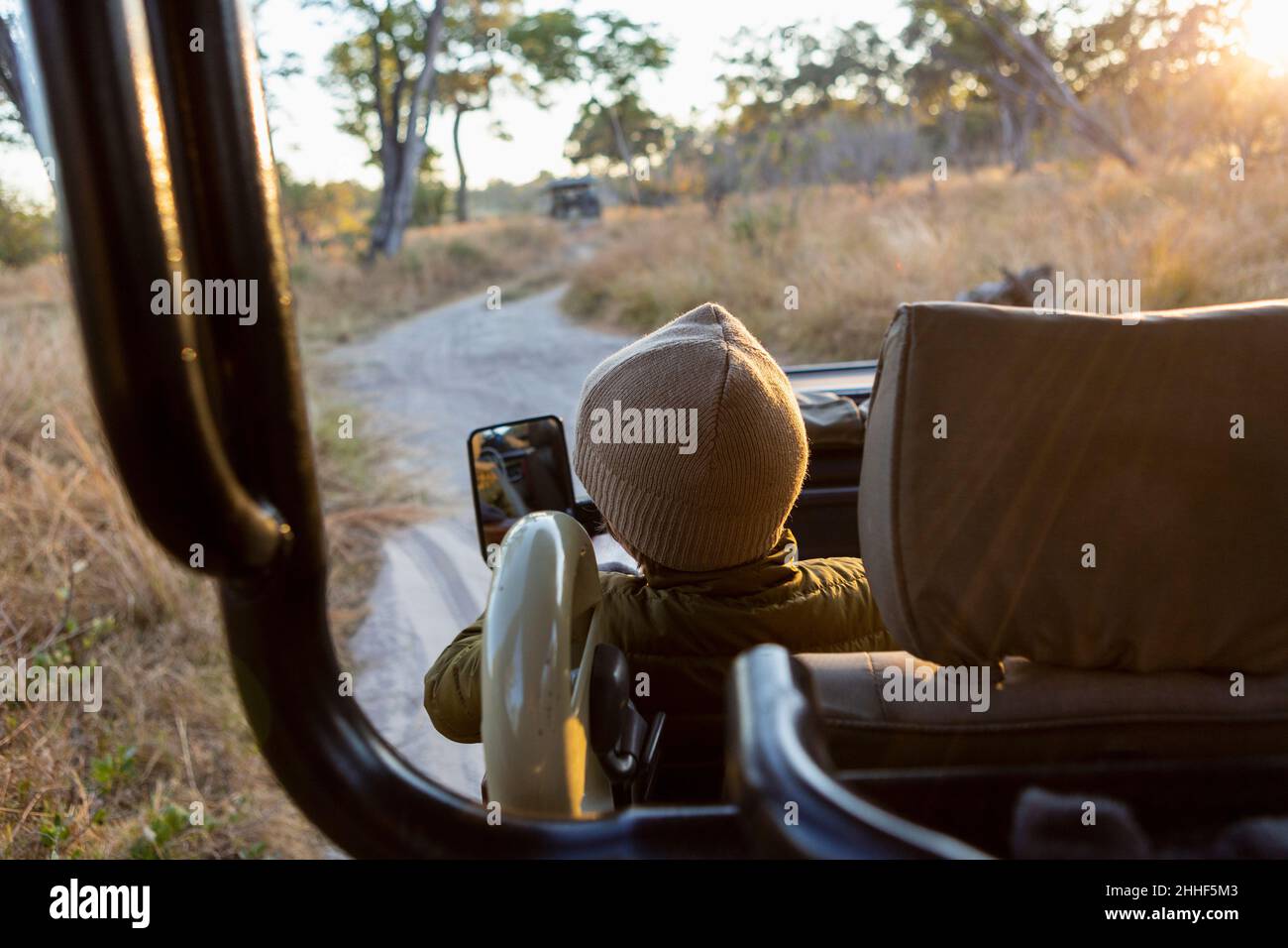 Un jeune garçon assis dans une jeep sur un safari au lever du soleil. Banque D'Images