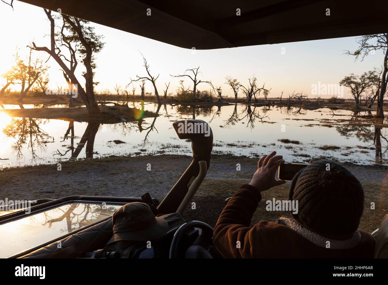 Personne assise dans une jeep en regardant le soleil se lever au-dessus de l'eau. Banque D'Images