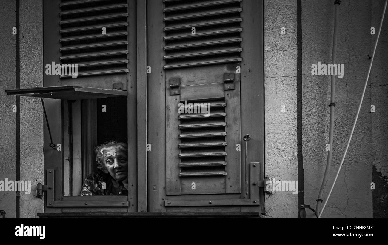 Eine alte, einsam wirkende Frau mit faltigem Gesicht schaut gedankenverloren aus ihrer auf eine Straße in Ajaccio herunter Banque D'Images