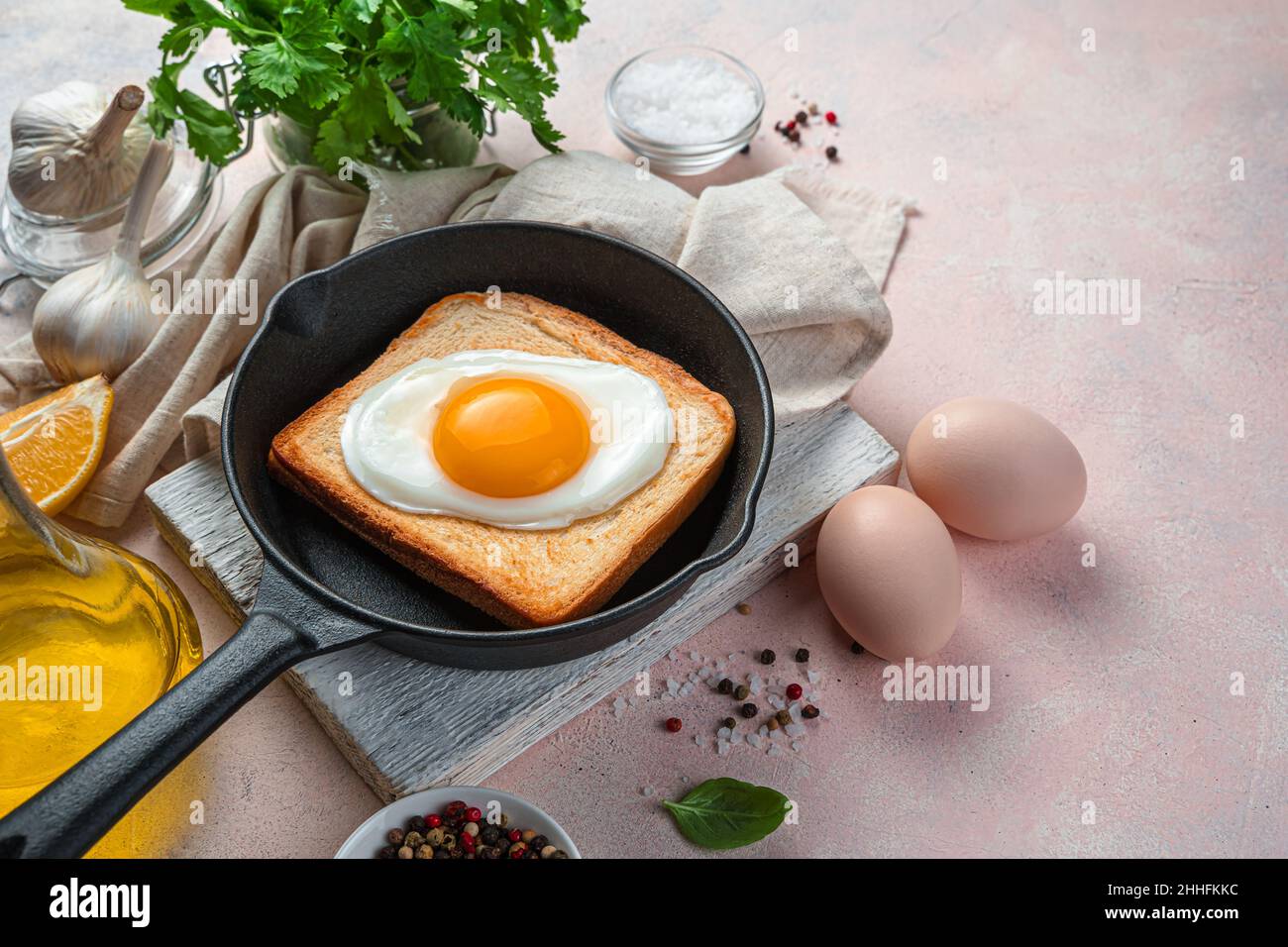 Œuf frit sur du pain grillé dans une poêle sur fond clair avec des épices et des herbes fraîches. Banque D'Images