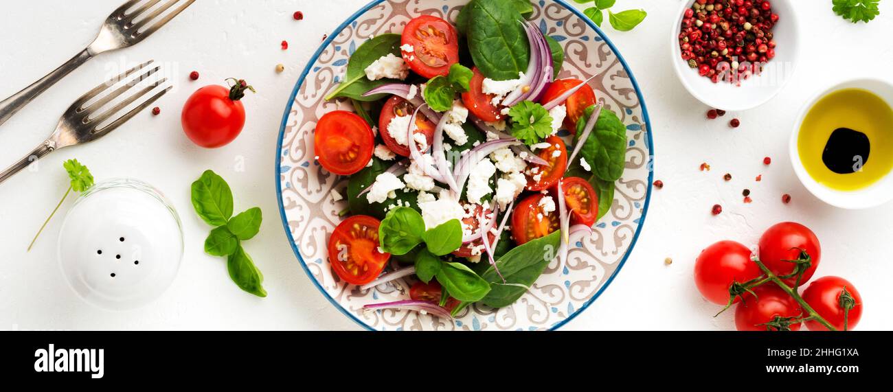 Tomates, feuilles d'épinards, oignons rouges et salade de feta sur une assiette en céramique légère.Mise au point sélective.Vue de dessus. Banque D'Images