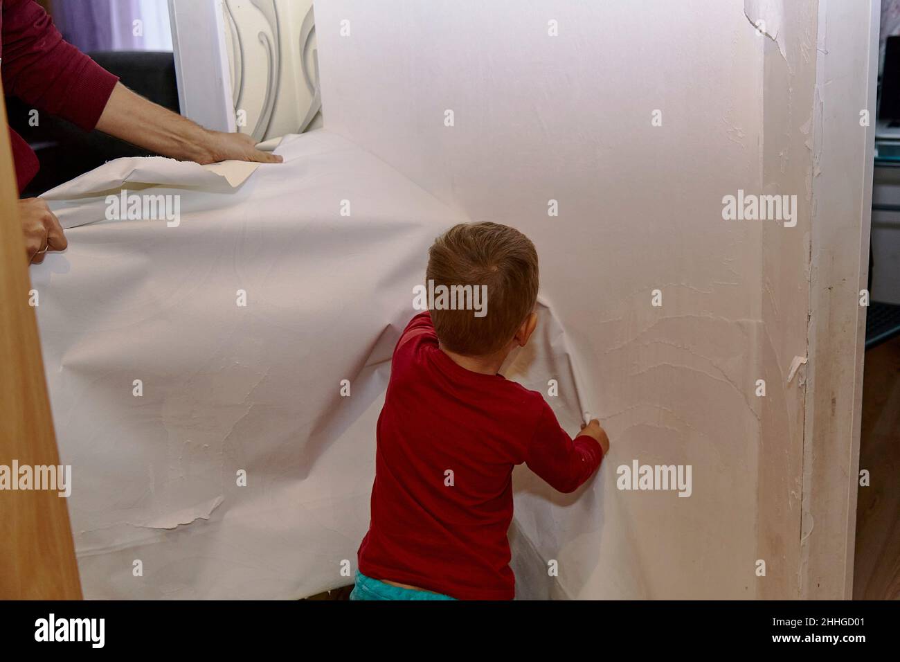 Le père et le fils retirent l'ancien papier peint du mur.Préparation pour la rénovation de la salle.Fils enseignant, bonne parentalité.Tâches ménagères.Papa et son jour ensemble. Banque D'Images