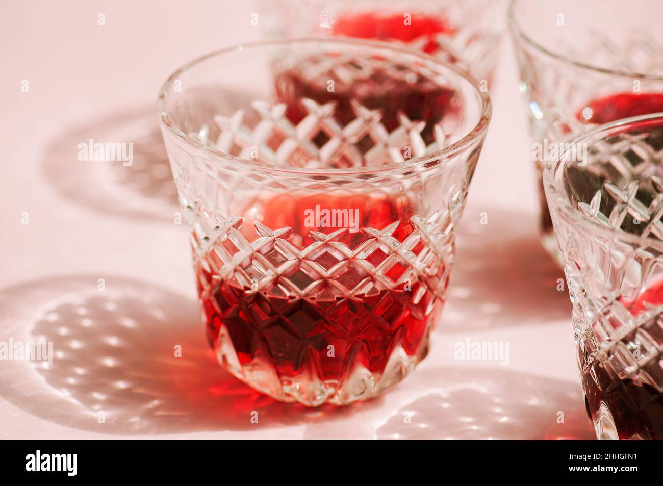 Vin rouge dans un verre transparent avec des ombres abstraites sur fond rose. Banque D'Images