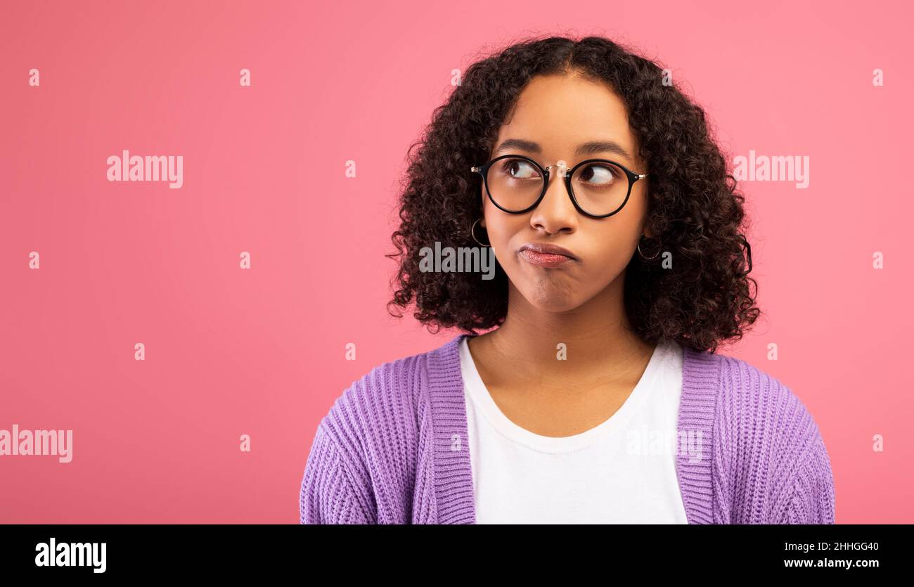 Jeune femme noire pensive dans des verres regardant l'espace de copie sur fond rose studio, conception de bannière Banque D'Images