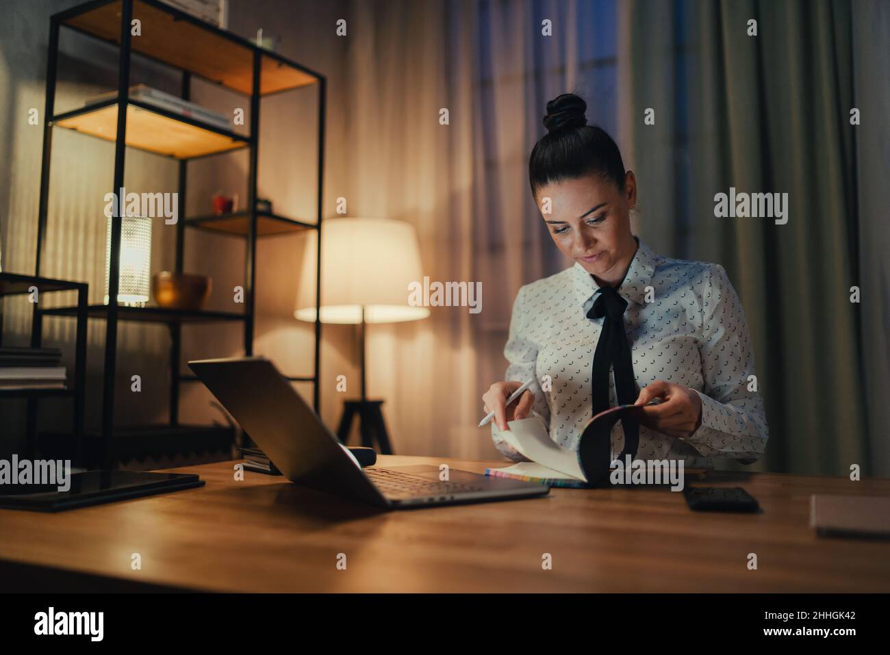 Bonne femme d'affaires de taille moyenne avec un agenda travaillant sur un ordinateur portable au bureau la nuit. Banque D'Images